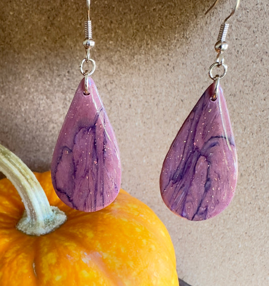 Butterfly Wing large teardrop-shaped polymer clay dangle earrings. Colors of Mauve and dark purple with rose gold foil flakes. Rose gold colored hooks and rings. Pumpkin in the background. 
